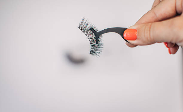 A hand holding a false eyelash applicator with lashes attached