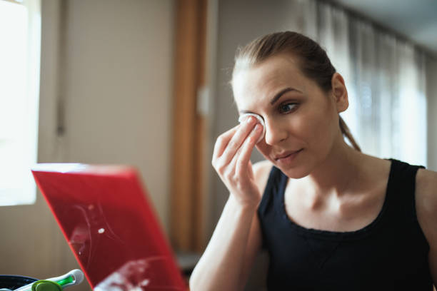 A close-up of a woman gently removing false lashes using cotton pads.