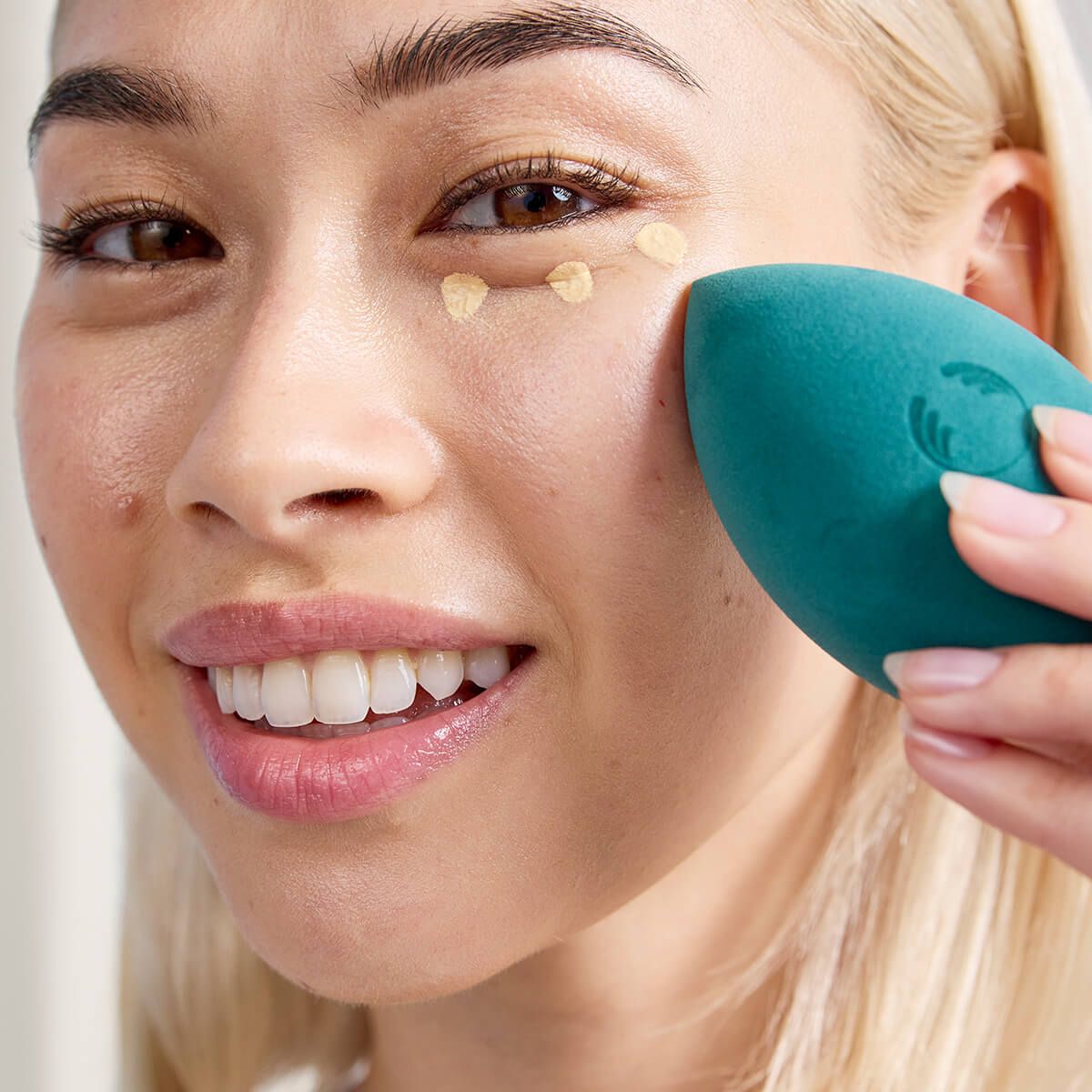 Woman applying peach color corrector before foundation for even tone.